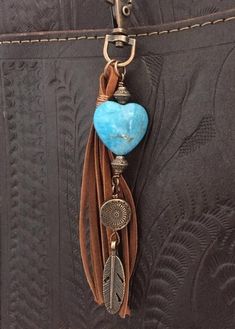 a leather purse with a blue heart and feather charm hanging from it's side