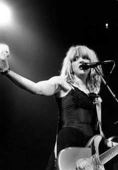 a woman in black dress singing into a microphone and holding her hand up to the side