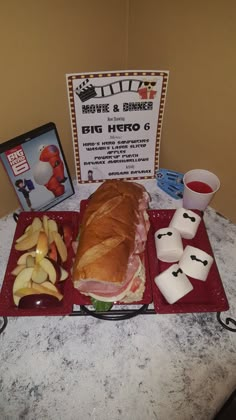 a sandwich and dice sit on a red tray next to other food, including apples