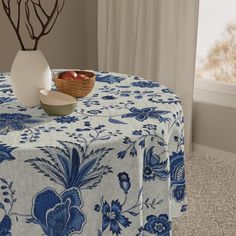 a blue and white table cloth with flowers on it next to a bowl of fruit