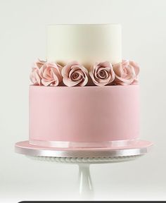 a three tiered cake with pink flowers on top and white frosting, sitting on a pedestal