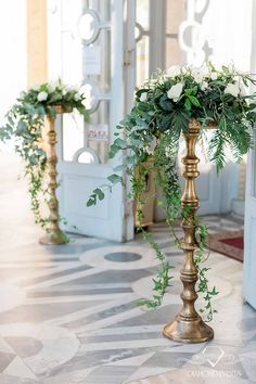 two tall gold vases filled with flowers and greenery on top of a marble floor