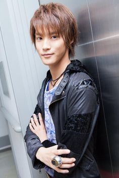 a young man standing in front of a metal wall with his arms crossed and looking at the camera