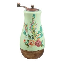 a green ceramic soap dispenser with flowers painted on the side and wooden handle