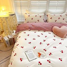 a white bed with cherries on it in a bedroom next to a lamp and window