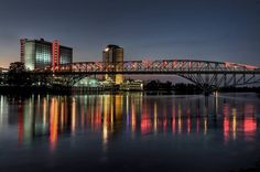 a bridge that is over some water with buildings in the background and lights on it