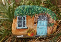 a rock with a house painted on it sitting in the grass next to some plants