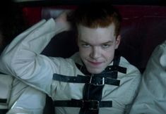 a man with red hair sitting in the back seat of a car wearing leather harnesses