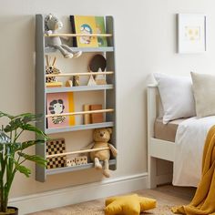 a white book shelf filled with lots of books next to a bed and potted plant