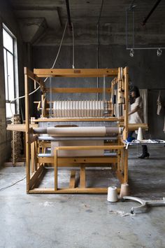 an old weaving machine is sitting in the middle of a room with two people working on it