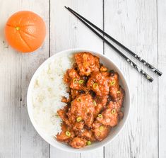 a bowl filled with meat and rice next to chopsticks on a white table