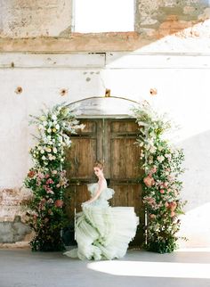 a woman in a green dress is standing by an open door with flowers on it