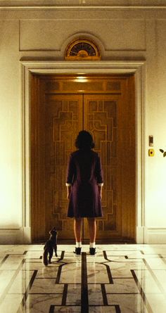 a woman standing in front of a door with a dog sitting on the floor next to her