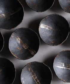 many black bowls are lined up together on the table, some with brown lines painted on them