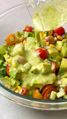 a bowl filled with vegetables and dressing being poured into the salad mixture in a large glass bowl