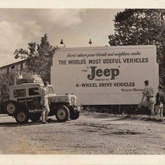 two men standing in front of a jeep with a sign on it's side