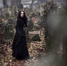 a woman in a black dress is walking through the woods with her hands on her hips