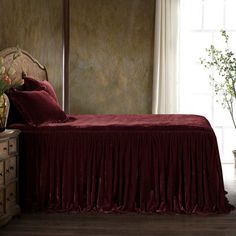 a bed with red sheets and pillows next to a vase filled with flowers on top of it