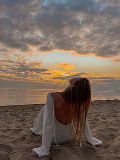 a woman sitting on top of a sandy beach next to the ocean under a cloudy sky