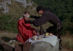 a man and woman sitting on top of a rock next to each other