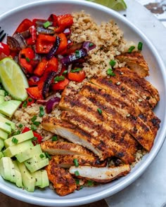 a white bowl filled with chicken, rice and veggies next to a fork