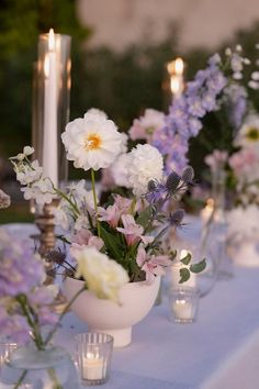 the table is set with candles and flowers in white vases on blue linen covered tables