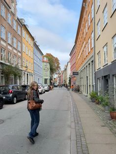 a woman is walking down the street in front of some buildings with cars parked on both sides