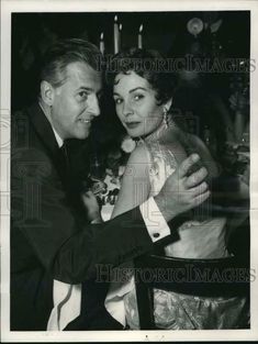 an old black and white photo of a man hugging a woman in a chair at a party