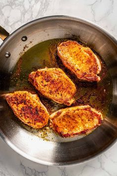 three pieces of chicken cooking in a frying pan on a marble counter top,