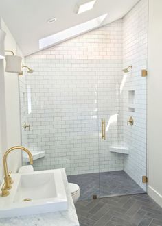 a bathroom with a walk in shower next to a white toilet and sink under a skylight