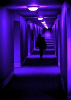 a person walking down a long hallway with purple lights