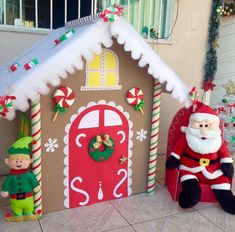 two christmas decorations in front of a gingerbread house with santa and elf figures next to it