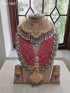 an elaborate necklace and earring set on display in front of a window with a wooden stand