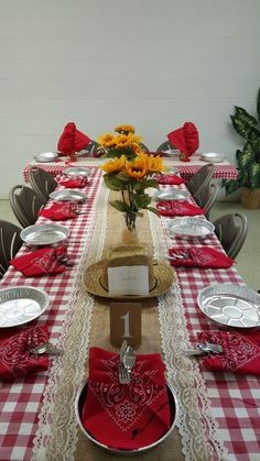 the table is set with red and white checkered linens, silverware, and flowers