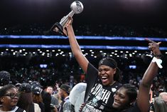 a woman is holding up a trophy in the air with other people around her at a basketball game