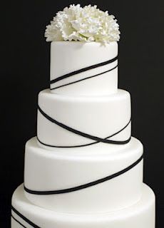 a white wedding cake with black ribbon and flowers