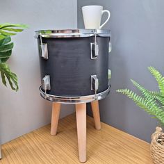 a black drum stands next to a potted plant on top of a wooden table