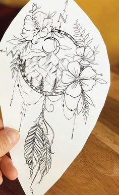 a person holding up a piece of paper with flowers and feathers on it in front of a wooden table