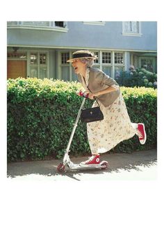 an old woman riding a scooter down the street in front of a house