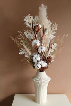 a white vase filled with lots of dried flowers