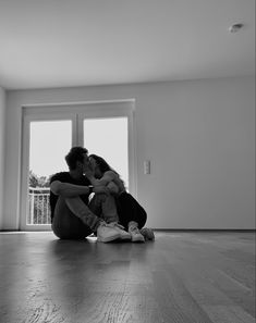 a man and woman sitting on the floor in front of an open window hugging each other