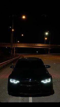 a black car is parked on the side of the road at night with its lights on