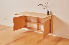 a small wooden table with an open door on the bottom shelf and a flower in a vase on top