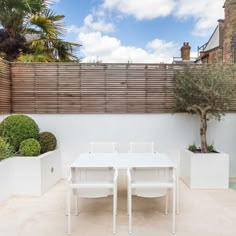 a white table and chairs sitting on top of a patio next to a small tree