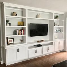 a living room with white bookcases and a flat screen tv mounted on the wall