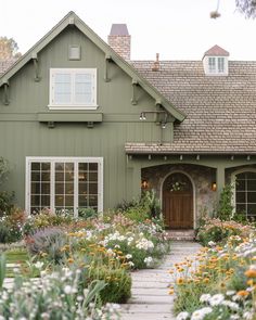 a green house with lots of flowers in the front yard and walkway leading to it