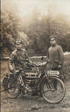 two men are standing next to an old fashioned motorbike and another man is sitting on the bike