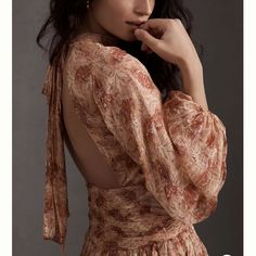 a woman in a floral dress poses for the camera with her hand on her chin