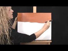 a woman with long hair painting on an easel in front of a black background