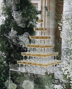 there is a tall glass cake on display in front of some trees and bushes with white flowers